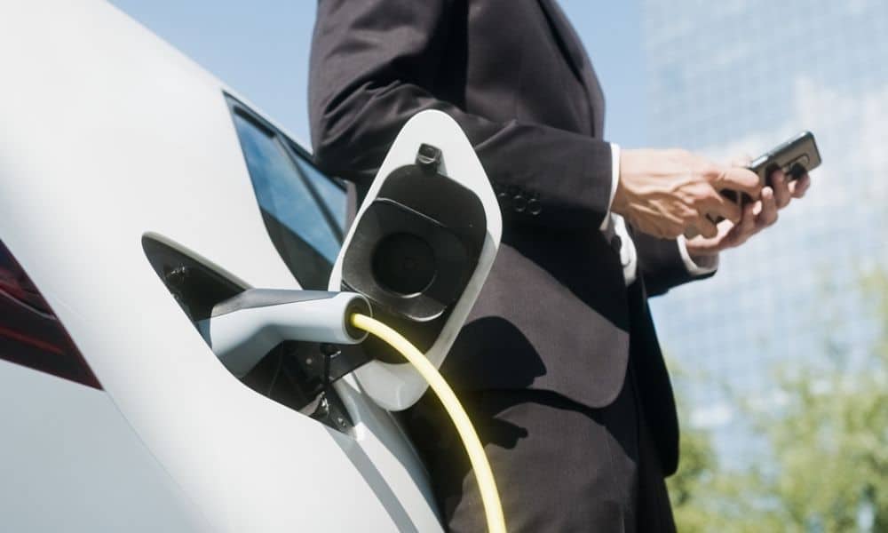 A businessman checking his phone while he waits for his EV to charge